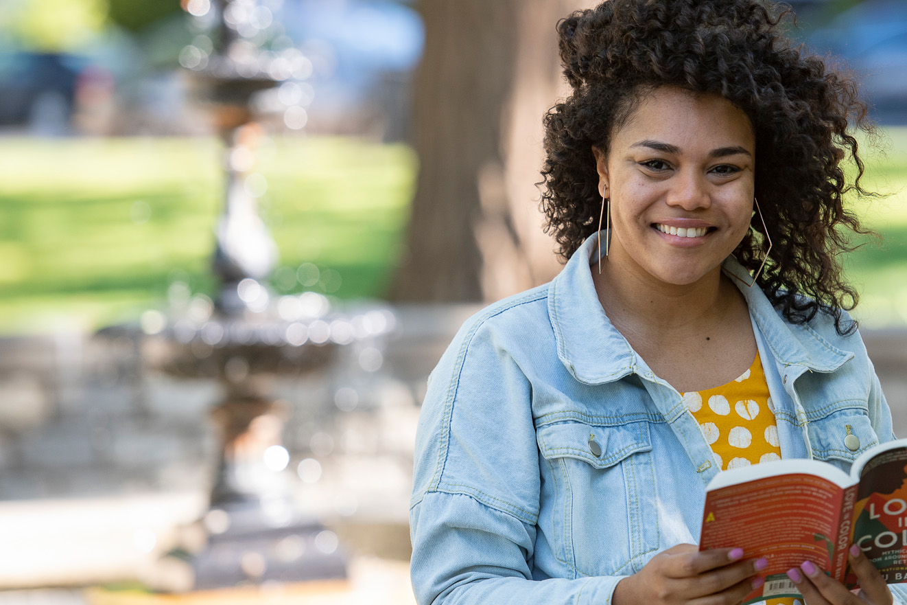 Christine Singleton holds a book outside with a fountain in the background
