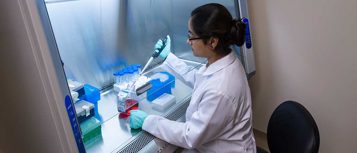 A student in a lab coat uses a pipette to drop liquid into a container in a chemistry lab