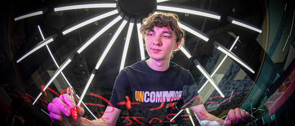 A student does a math equation on clear glass in the STEM Building's Math Exchange