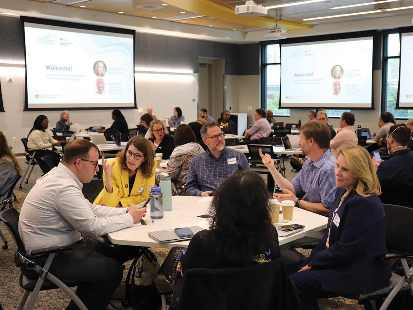 Faculty members sitting around tables in a large room, having conversations