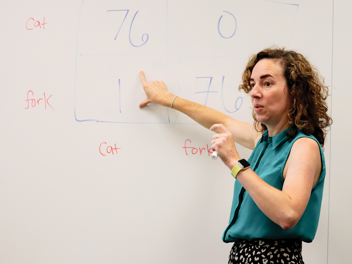 A professor stands in front of a whiteboard, pointing to numbers written on the board
