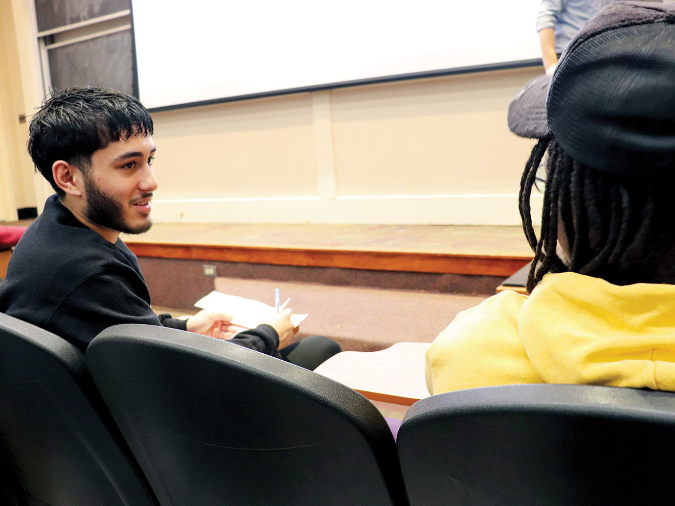 Two students talk to one another from theirs seats in a lecture hall