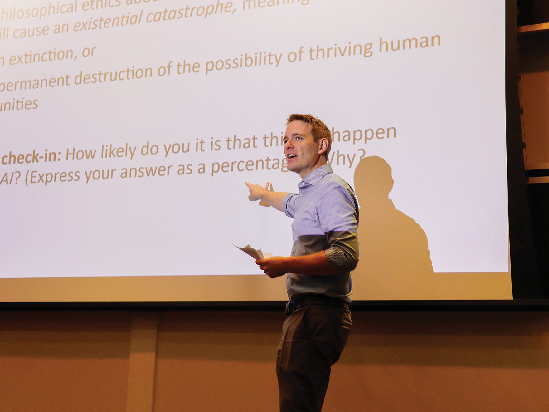 A professor stands in front of a classroom, pointing to notes projected onto a screen