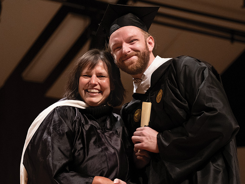 A man and woman in graduation regalia pose for a photo