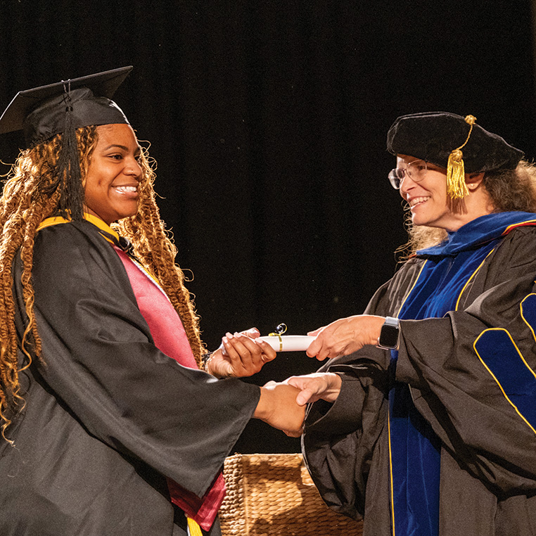 A student in graduation regalia receives a diploma from a faculty member in regalia