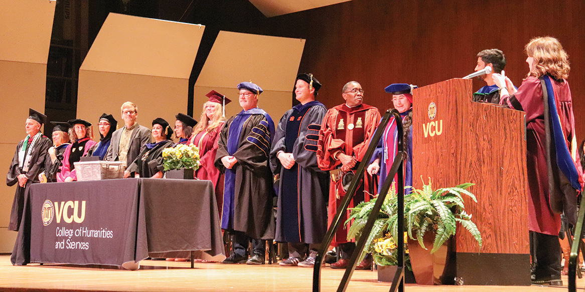 VCU faculty in graduation regalia line up on stage at a commencement ceremony