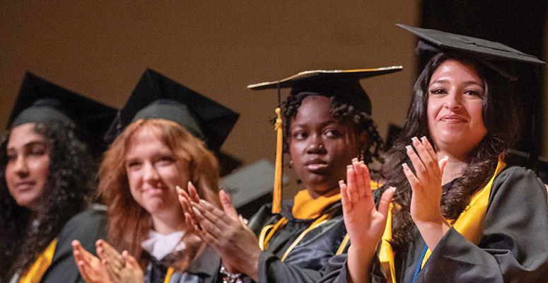 Four students in graduation regalia clapping their hands