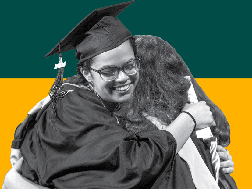 Two students in graduation regalia embrace each other