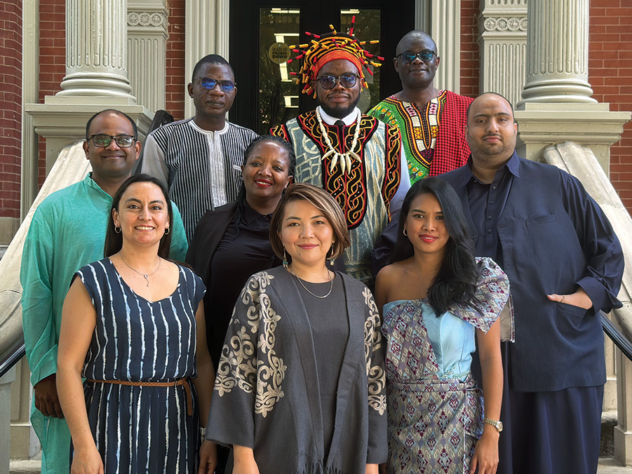 Nine Humphrey Fellows stand for a group photo on the steps outside of a brick building