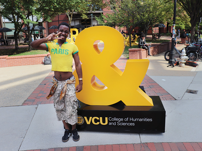 A student poses in front of a gold ampersand statute on VCU's campus