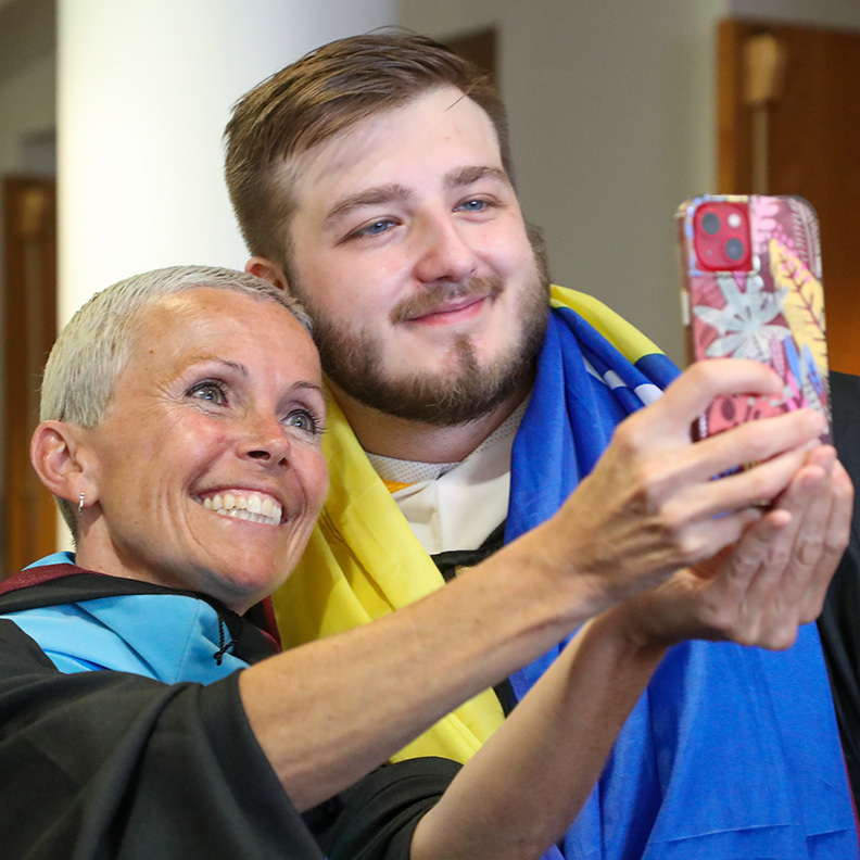 A graduate and a professor pose for a selfie