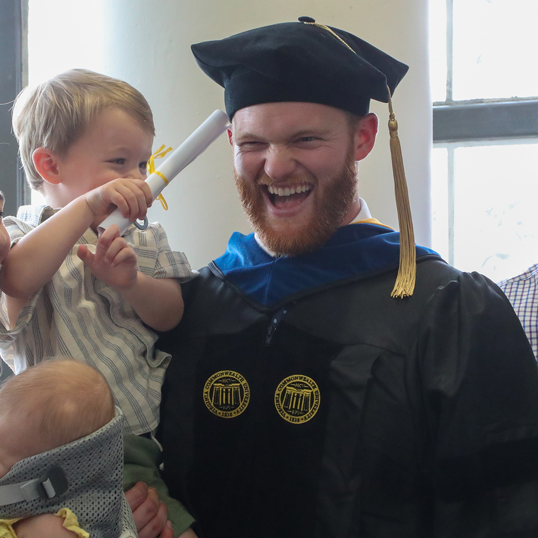 A smiling graduate holds a toddler