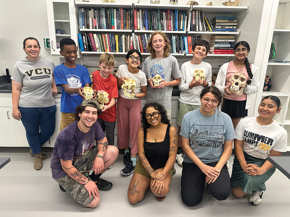 A group of middle school students hold up 3D printed skulls in a college classroom