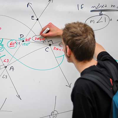 a student solving math problems on a white board