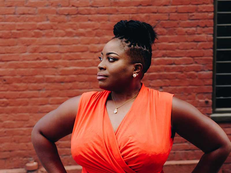 woman with hands on hips in front of brick wall