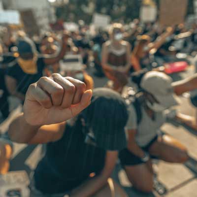 masked people at a rally raising fisted hands and bowing their heads