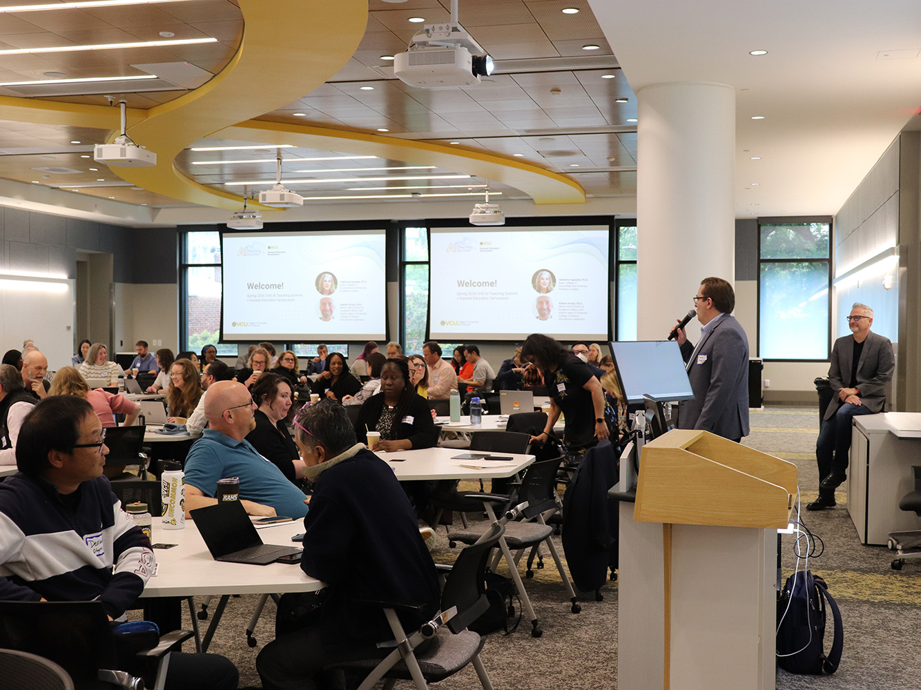 Associate Dean Marcus Messner speaks in front of a conference room full of attendees