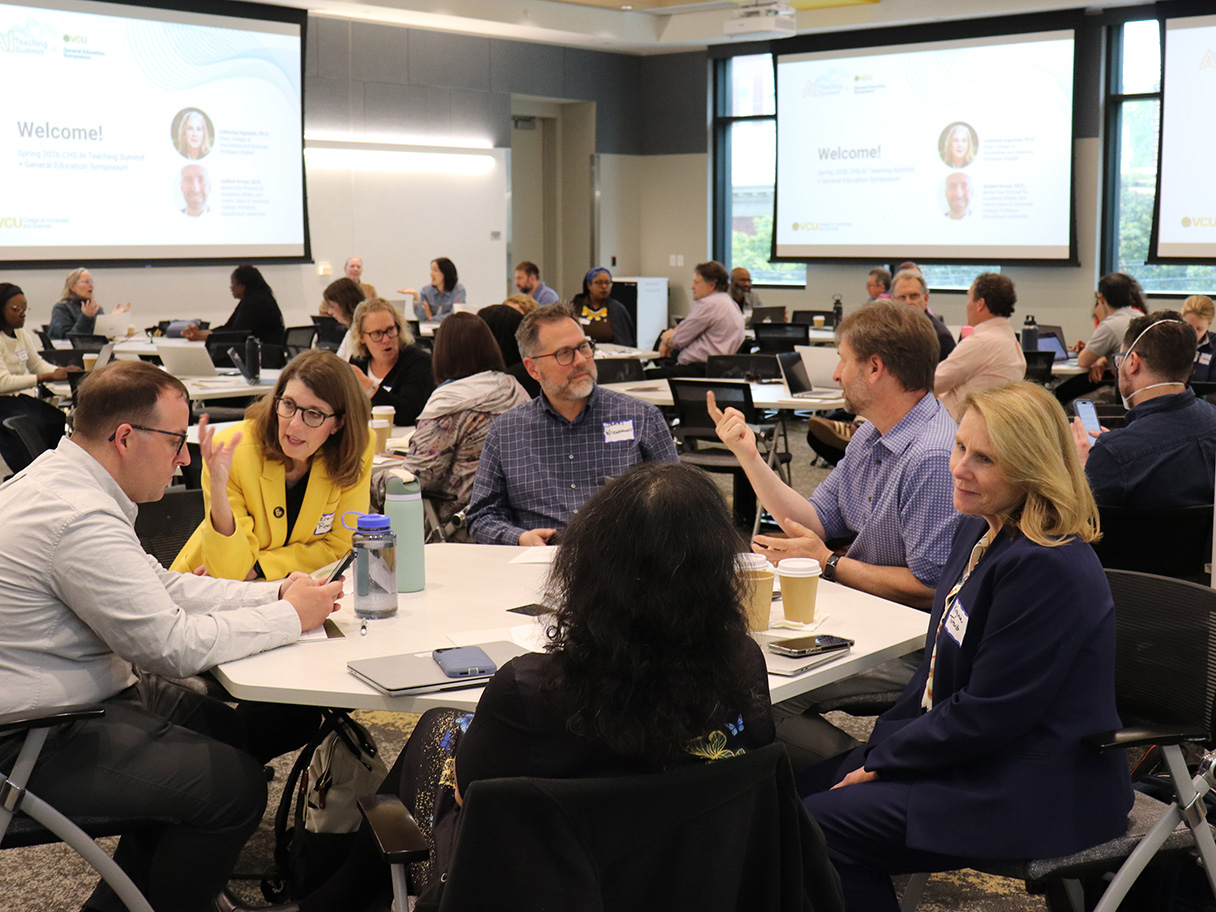 Groups of attendees sit at tables in a conference room