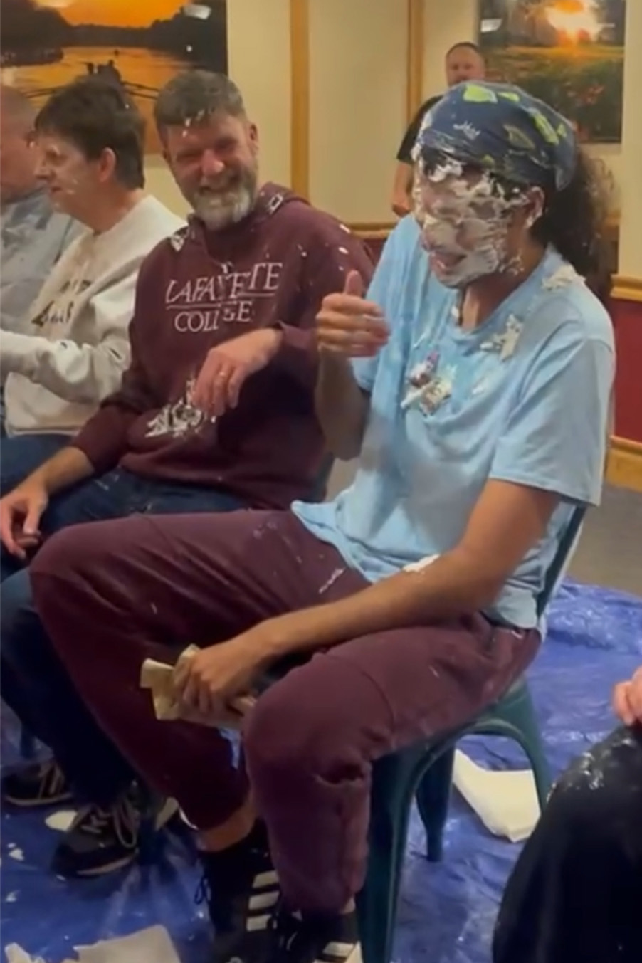 Rayan Ibrahim sits in a chair next to others, laughing with frosting on his face