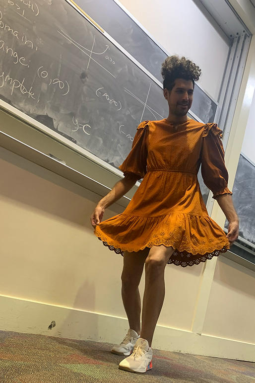 Rayan Ibrahim, stands in front of a chalkboard in an orange dress