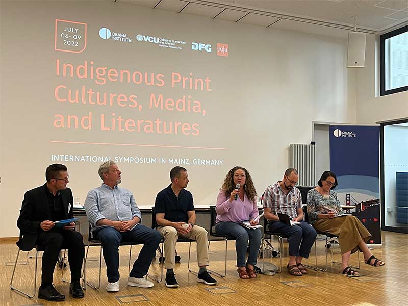 A panel of speakers sitting in front of a large wall with the words: 