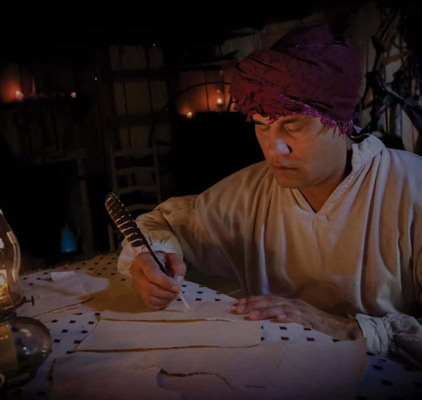 a person writing on a piece of paper with a feather pen.