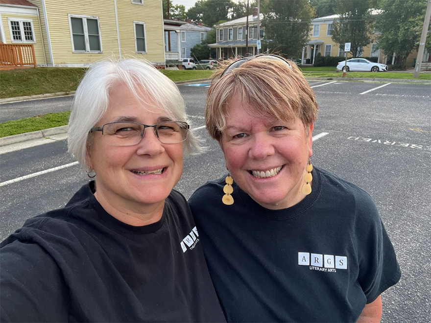 Patty Smith and another woman take a selfie on road with a building behind them