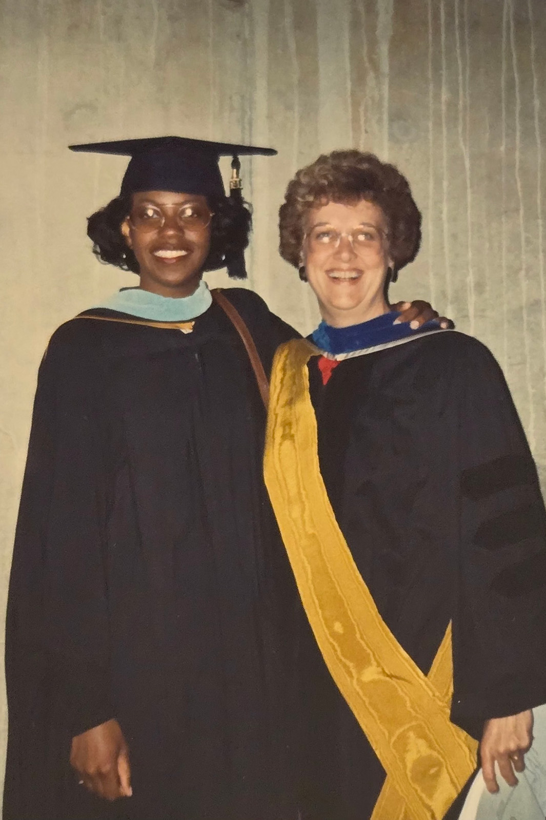 Adriene Marshall and and another woman stand beside each other in graduation regalia