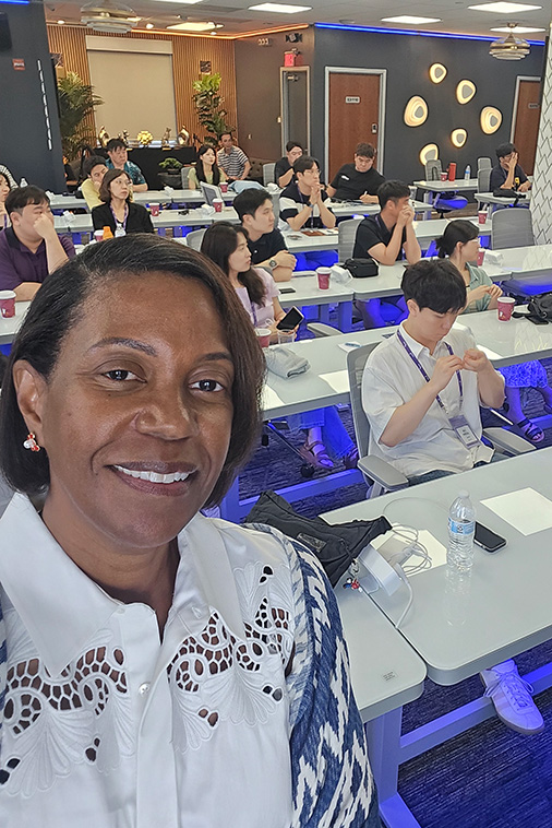 Adriene Marshal takes a selfie in front of a classroom full of students sitting at desks